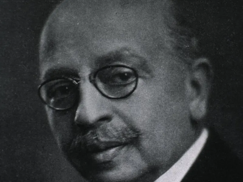 An old black-and-white portrait of a man with a moustache and round glasses