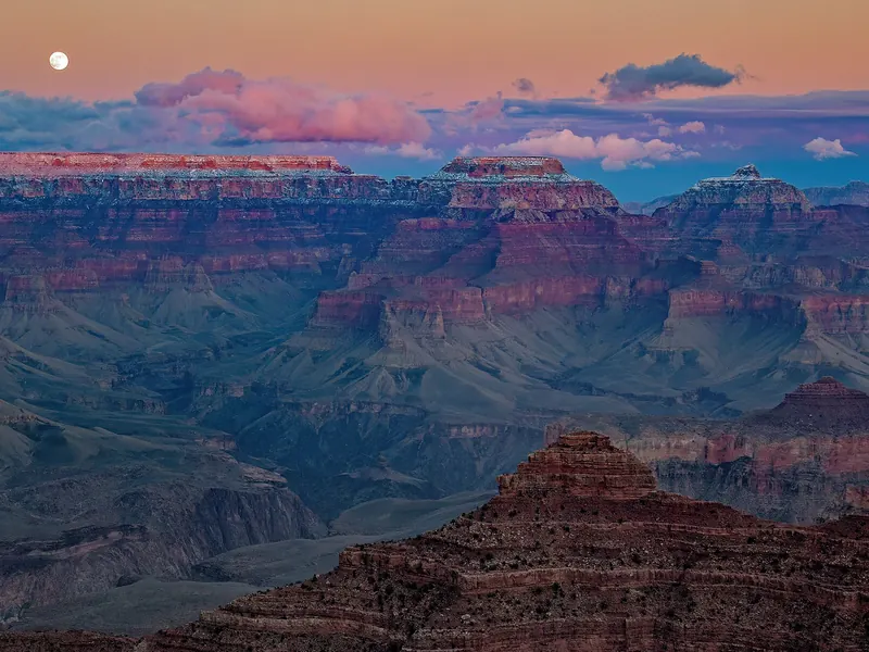 A full moon rising over the layered cliffs of a canyon at dusk