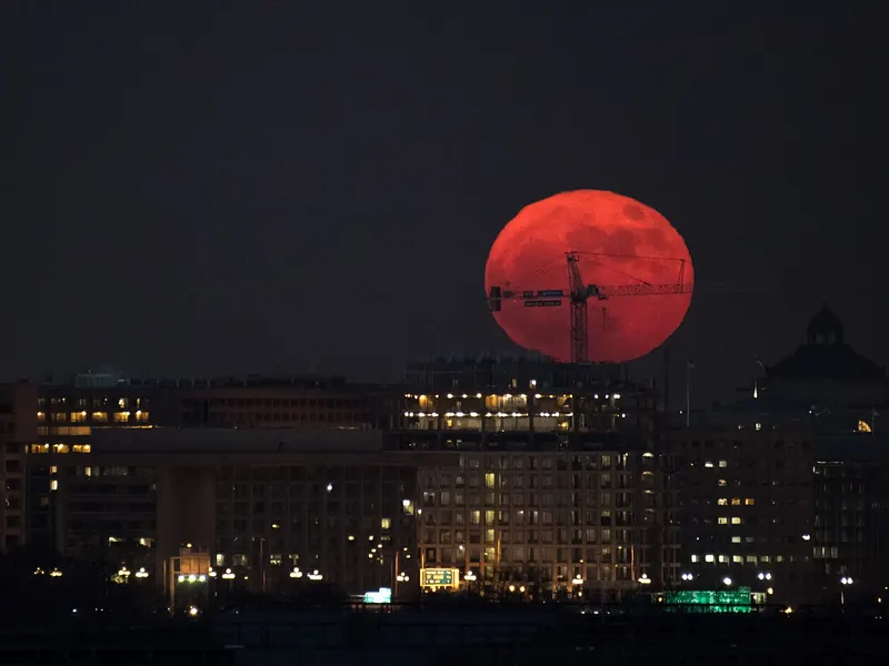 A huge orange full moon rising behind the dome of a city building at dusk